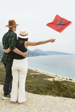 Couple travelers on viewpoint holding Albanian flag travel Albanian Riviera coastline. National celebration freedom patriotism Vlore Albania