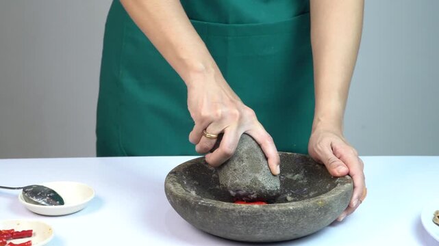 Woman grinding red chili peppers and spices using traditional stone mortar and pestle