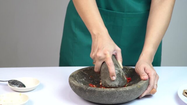 Woman grinding red chili peppers using a traditional stone mortar and pestle