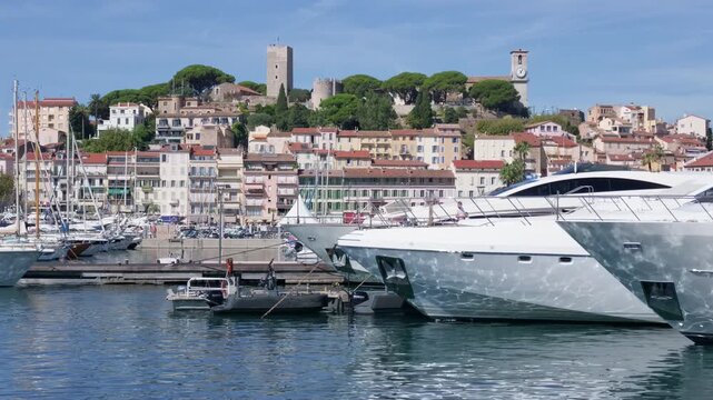 Wide view of a marina with sailboats, a small tender boat and hillside old town in the background, Cannes, France