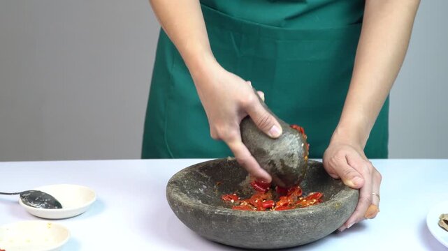 Woman in green apron grinding chili peppers with stone mortar and pestle