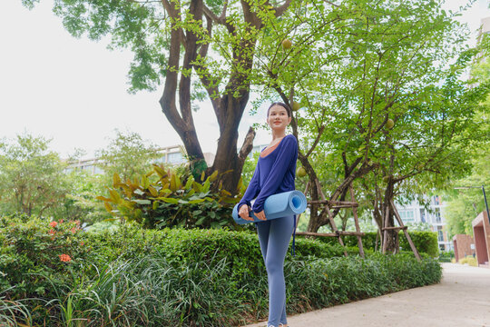 Asian Gen Z woman carrying yoga mat walking to park for wellness healthy lifestyle mindfulness and outdoor exercise.