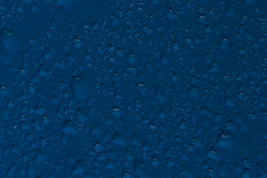 Dense water droplets and trails on a dark blue surface in horizontal view.
