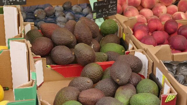 Fresh avocados and nectarines displayed in cardboard boxes at an outdoor market stall