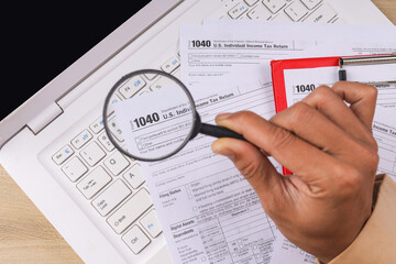 Obraz premium Closeup of Hand Holding Magnifying Glass for US Individual Income Tax Return Form 1040 on Laptop