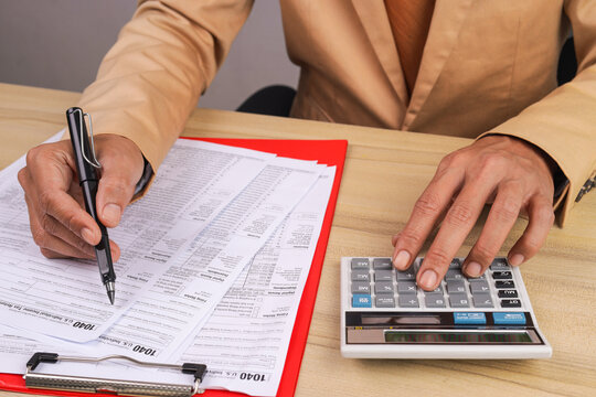 Businessman Holding Pen and Using Calculator to Fill Out Tax Return Forms
