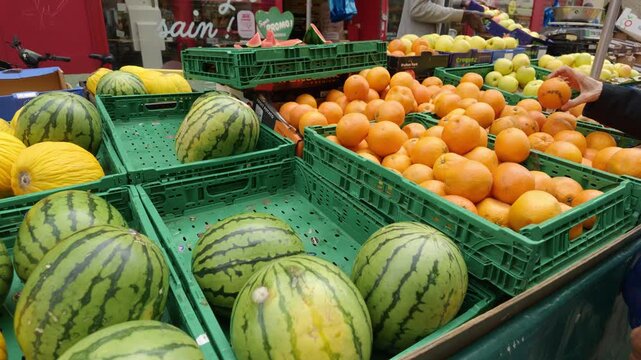 Vendor displaying watermelons, oranges, and cantaloupes at an outdoor market stall