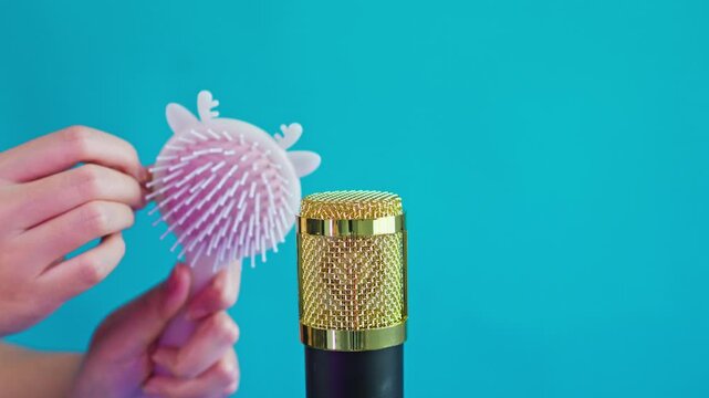 Close-up of fingers scraping paddle hairbrush near condenser microphone in studio setting