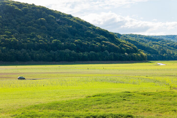 Obraz premium Car driving across the exposed grassy bed of Domaša reservoir in Slovakia, with the Ondava River flowing through the drained landscape during extremely low water levels.
