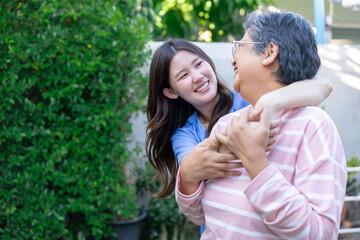 Fototapeta premium Happy young daughter and senior mother hugging and smiling outdoor in green garden showing joyful emotion and beautiful family bonding