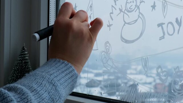 Sustainable responsible holiday decor. Female hand painting snowman painted on window glass indoor at home. Christmas winter decoration. White pattern. Snow art tracery on season. Diy. Hygge home