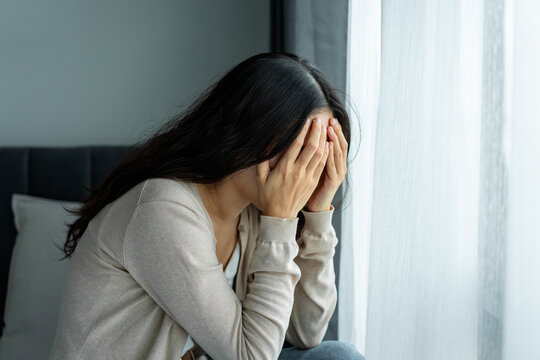 Depressed young Asian woman covering her face with hands in sadness at home, Mental health problems and depression concept