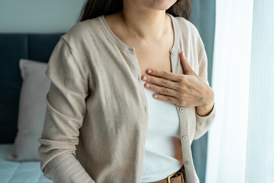 Asian female holding her chest, feeling discomfort from acid reflux and heartburn