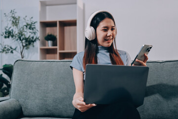 Beautiful young asian woman sitting on sofa and holding joystick playing online video game in living room at house © ARMMY PICCA