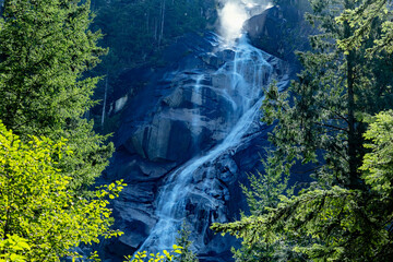 Majestic waterfall cascades down a dark, rocky cliff face surrounded by lush green trees, Shannon Falls Viewpoint, BC, Canada © Rajesh