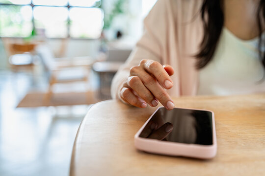 Close-up of a smiling woman swiping on a mobile phone screen on a wooden desk, cozy cafe background.