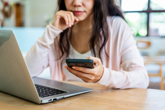 Cropped shot of a thoughtful Asian woman resting her chin on hand while working on laptop at a bright home desk