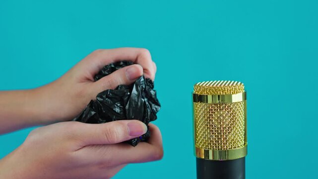 Hands crumpling black plastic bag near studio microphone 