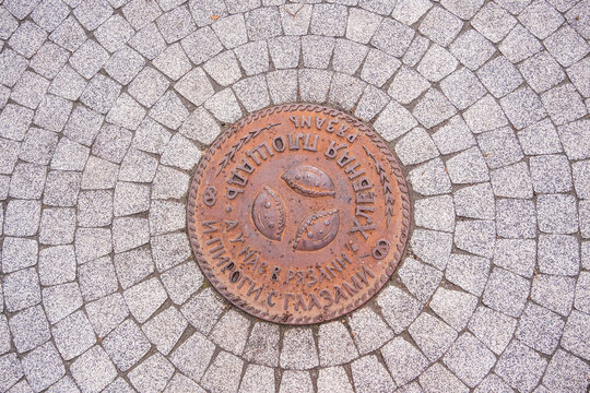 Round metal plate with text and three pie shapes on a stone pavement. Circular design on cobblestone road for urban ground texture.