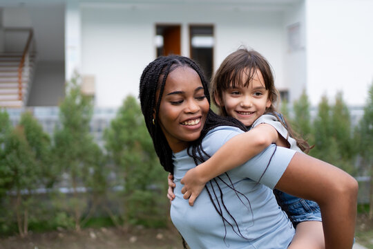 African nanny carrying and playing with young child outdoors in a garden. 