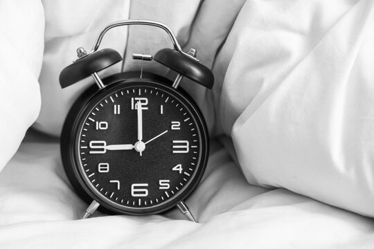 Black alarm clock with blanket on bed, closeup