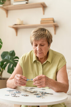 Senior woman actively engages her mind by putting together a puzzle on small table. Slow, mindful living, analog hobby, relaxing activity at home