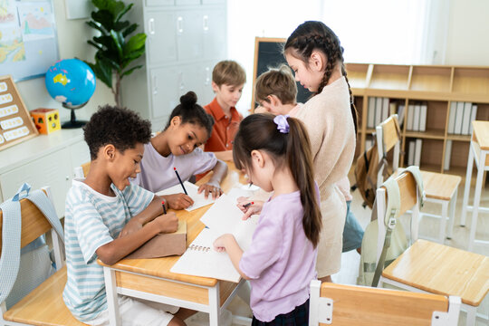 Group of diverse students folding paper on table at elementary school. 