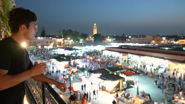 Marrakech, morocco. August 9, 2026. Young tourist enjoying a traditional mint tea on a balcony overlooking the bustling jemaa el fna market in marrakech at nightfall