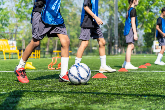 Close up of young children dribbling a football on outdoors sports field.