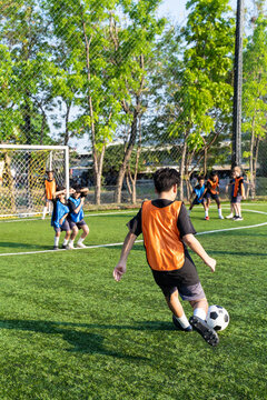 Young school children dribbling football on outdoor soccer field. 