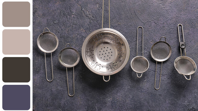 Culinary preparation and kitchen organization, stainless steel colander and various mesh strainers arranged on a dark textured stone background