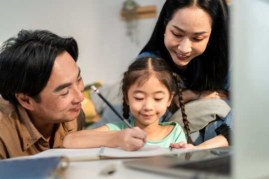 Asian loving couple support young kid daughter doing homework in house.