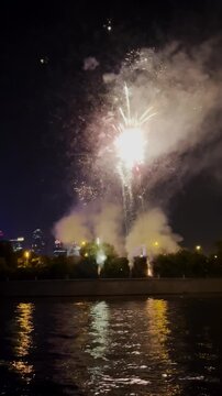 Fireworks exploding in the night sky over a city skyline and water. Celebration display for New Year's Eve or other holiday.