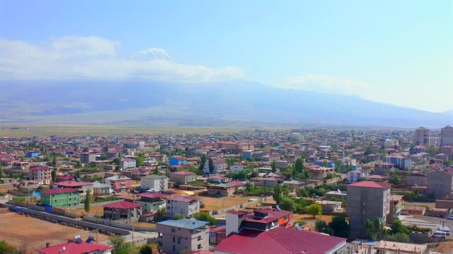 Drone flies forward above Dogubayazit rooftops and a long city boulevard with Mount Ararat on the horizon, supporting urban expansion, travel promotion, regional geography and eastern Turkey media.
