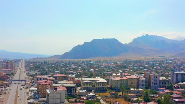 Drone flies forward above a city in eastern Turkey toward mountain ridges, showing broad avenues, dense neighborhoods and regional growth for travel, geography, infrastructure and tourism media.