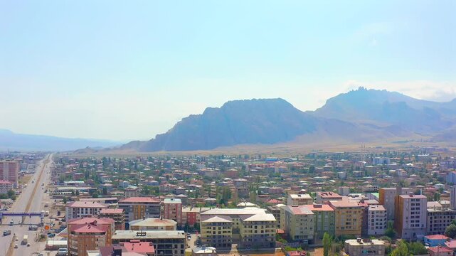 Drone flies forward above an eastern Turkish city toward rugged mountain ridges, showing housing, wide roads and urban expansion for regional travel, geography, planning and tourism content.