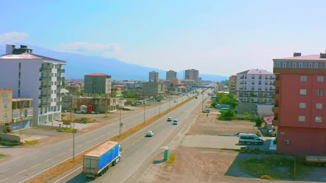 Drone flies forward above broad city avenue with Mount Ararat rising in the distance, showing traffic and urban districts in eastern Turkey for travel, transport, geography, destination tourism media