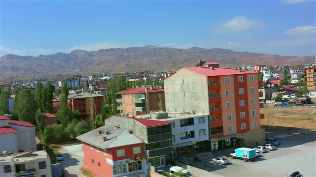 Drone descends above a residential neighborhood in eastern Turkey, showing apartment blocks, local streets and mountain terrain for housing, urban development, regional planning and travel media.