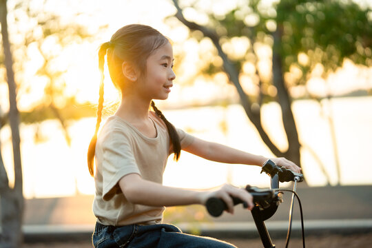 Asian young girl practicing riding a bicycle in a garden during sunset. 