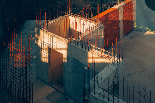 High-angle view of cast concrete walls and exposed steel rebar on a building construction site in warm sunlight.