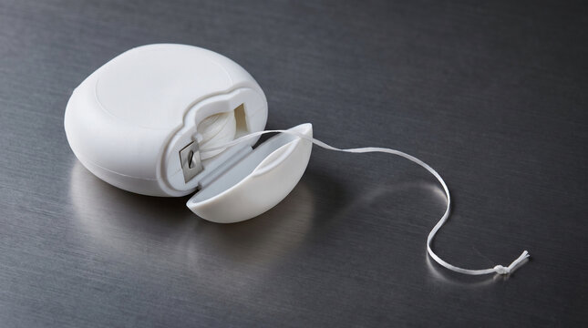 White Dental Floss Container with Thread on Brushed Metal Countertop Background Hygiene Concept
