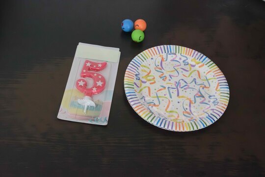 Birthday celebration items showing a colorful cake candle, a party plate, and bingo balls on a table