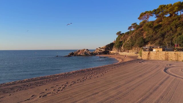Aerial view taken from a drone of the coast of Lloret de Mar, Costa Brava, Spain, early in the morning at sunrise - the sea, beach and coastal cliffs of the city bay
