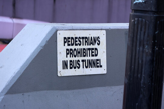 Close-up of a white street sign reading "Pedestrians Prohibited in Bus Tunnel" mounted on a gray grey concrete barrier