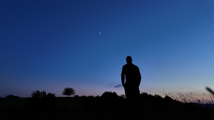 Silhouette of a person in nature observing night sky, Moon, stars and planets from a remote location. © astrosystem