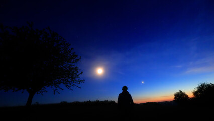 Silhouette of a person in nature observing night sky, Moon, stars and planets from a remote location. © astrosystem