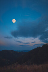 Full Moon, stars and planets above landscape silhouettes in blue hour time. © astrosystem