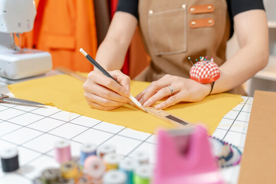 Professional fashion designer working in a modern sewing studio, measuring, marking and cutting fabric patterns for custom clothing production. Creative apparel development