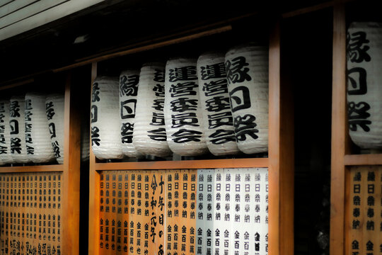 Row of traditional Japanese white paper lanterns (chochin) with black kanji characters hanging above wooden donor plaques at a shrine or temple festival
