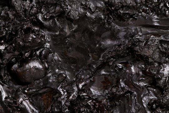 Dark surface with shiny texture found in a natural setting, possibly related to oil or tar deposits